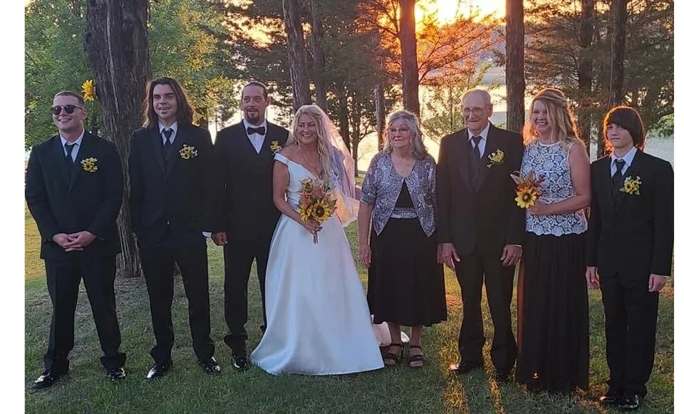 A wedding party poses outdoors at sunset with sunflower bouquets and formal attire.