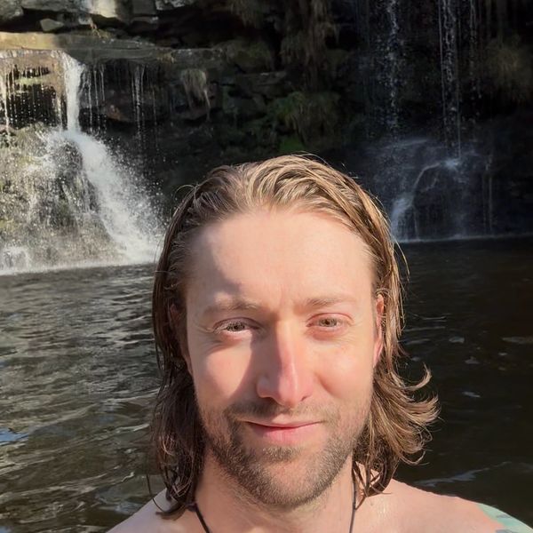 Breathwork Facilitator, Nathan, smiling in water with waterfall in background