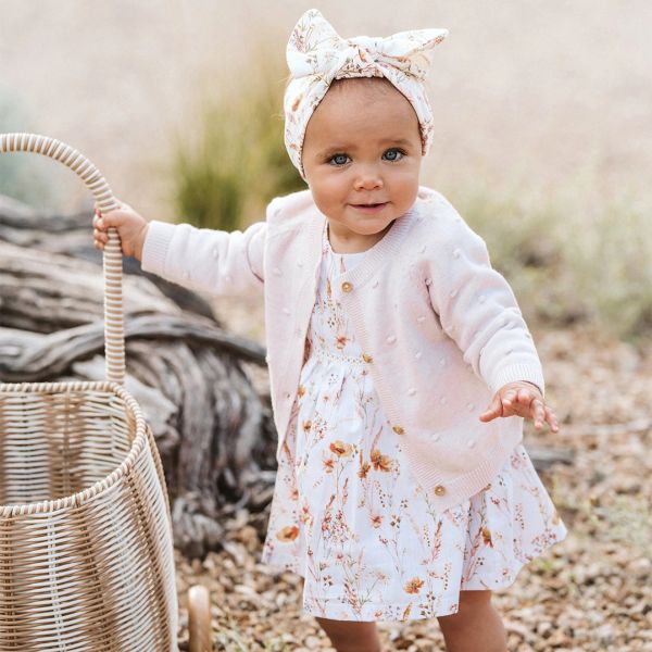 Toddler girl in floral dress and cardigan holding wicker basket.
