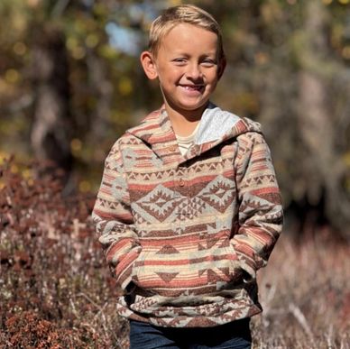 Smiling boy in a patterned hoodie outdoors, hands in pockets.