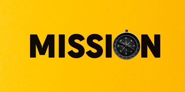 The word "MISSION" with a compass replacing the letter "O" on a yellow background.