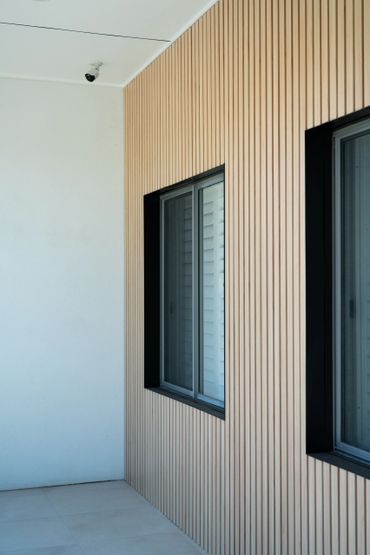 Modern wall with vertical wooden slats and two black-framed windows.