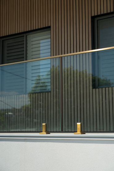 Modern glass balcony with gold fixtures on a wood-paneled building.