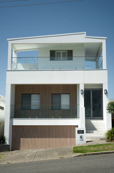 Modern two-story white house with wooden accents and glass balcony.