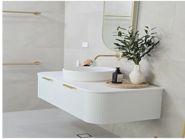 Modern white bathroom vanity with gold fixtures and a vase with green foliage.