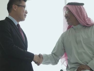 Two men, one in business attire and the other in traditional Middle Eastern clothing, shaking hands.