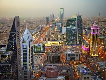 Aerial view of Riyadh's skyline with illuminated buildings at dusk.