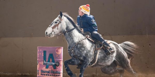 A rider in a colorful hat races a horse around a barrel indoors.