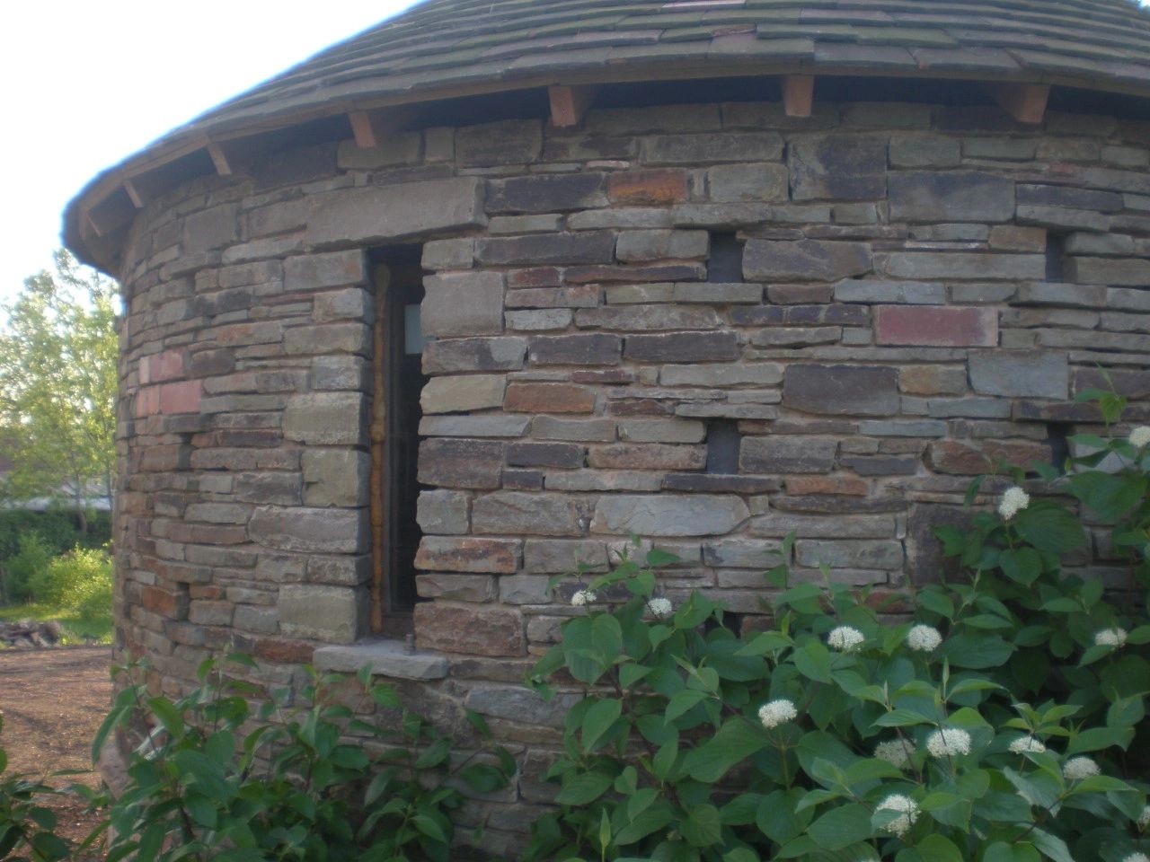 Round stone building with a small window surrounded by green plants.