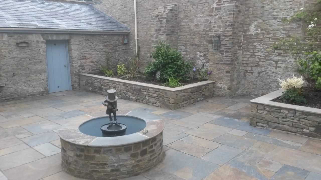 Quiet courtyard with stone walls, raised flower beds, and a small fountain featuring a statue.