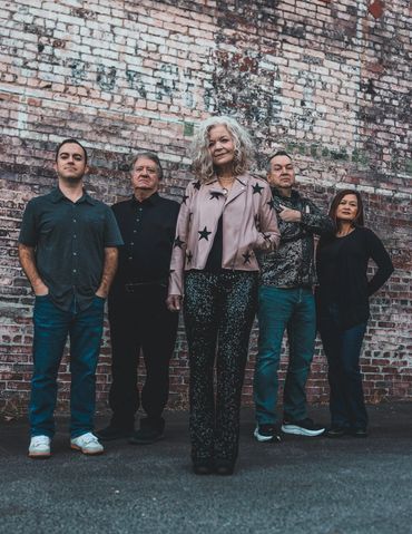 Five people posing confidently against a brick wall background.