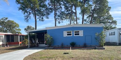 A small blue house with a carport and a yard.