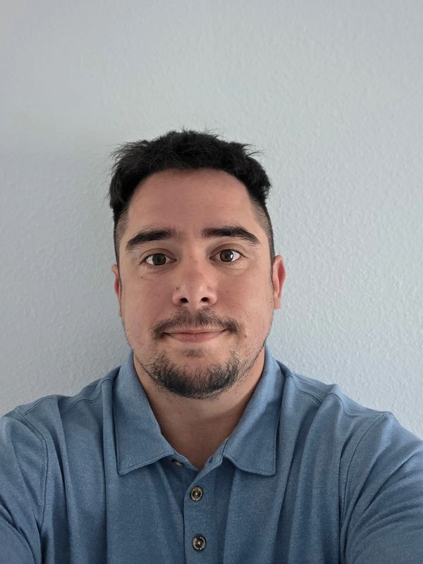 Man in a blue polo shirt smiling against a plain wall.