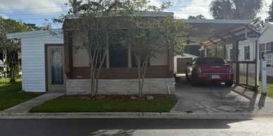 Small house with a carport and a red car parked outside.