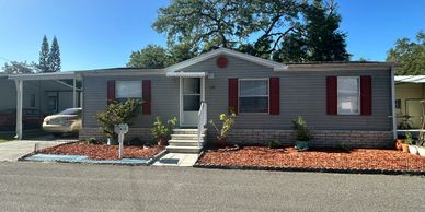 Single-story mobile home with red shutters and a small front porch.