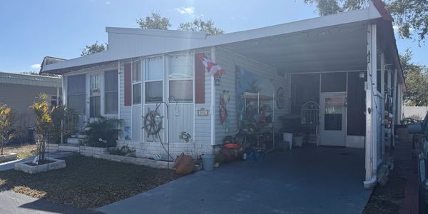 White manufactured home with a carport and nautical decorations on the wall.