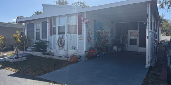 White manufactured home with a carport and nautical decorations on the wall.