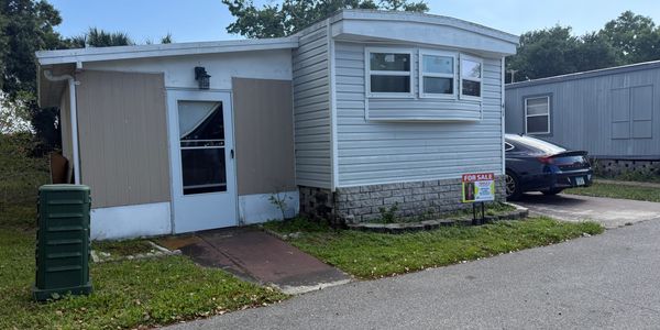A small mobile home with a car parked beside it in a residential area.