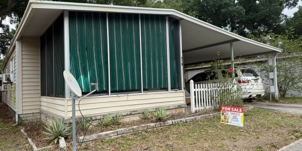 Mobile home with green striped awning and carport for sale.