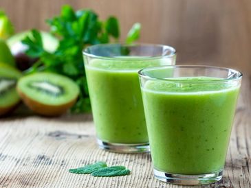 Two glasses of fresh green kiwi smoothie on a wooden table.