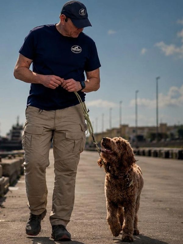 Man in casual outfit walking a happy brown dog on a leash outdoors.