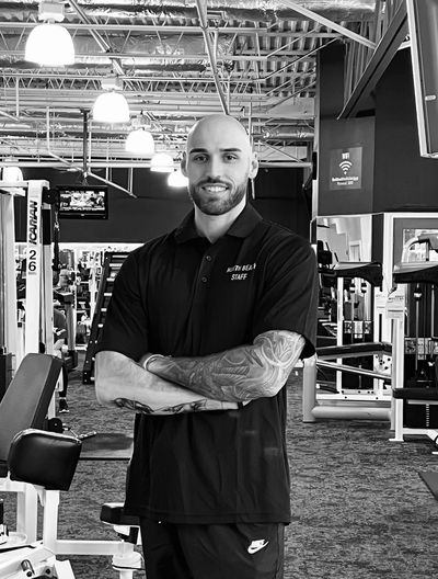 Confident gym staff with tattoos posing inside a fitness center.