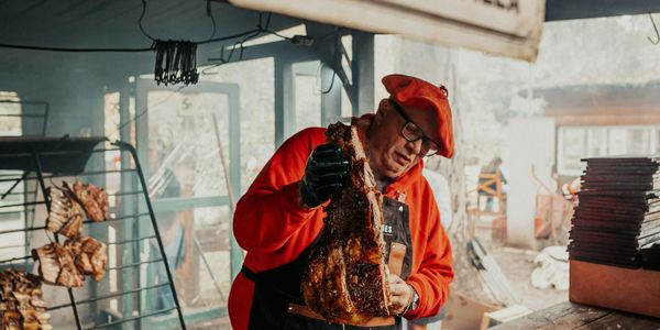A man in a red outfit holding grilled meat indoors.
