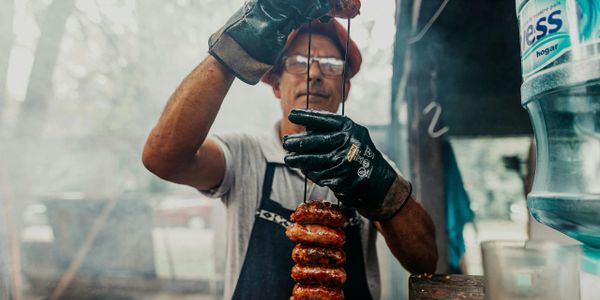 Man grilling sausages with protective gloves and apron.