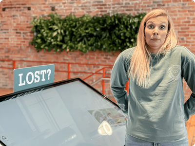Woman with a confused expression standing near a 'LOST?' sign and a digital map.
