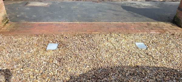 Gravel driveway with two metal access covers and a brick border.