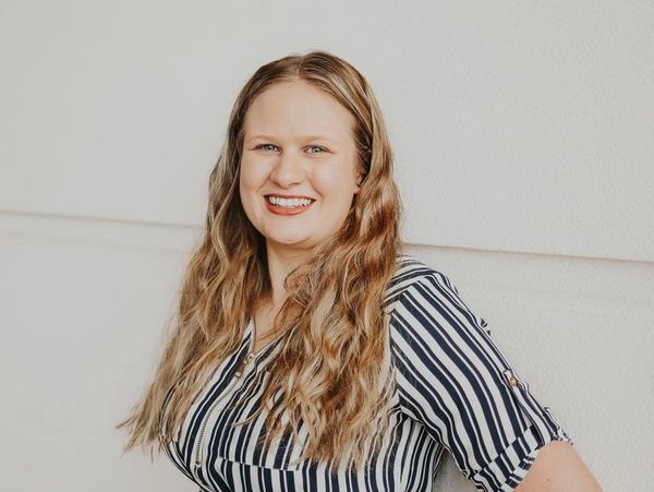 Woman with long wavy hair smiling, wearing a black and white striped shirt.