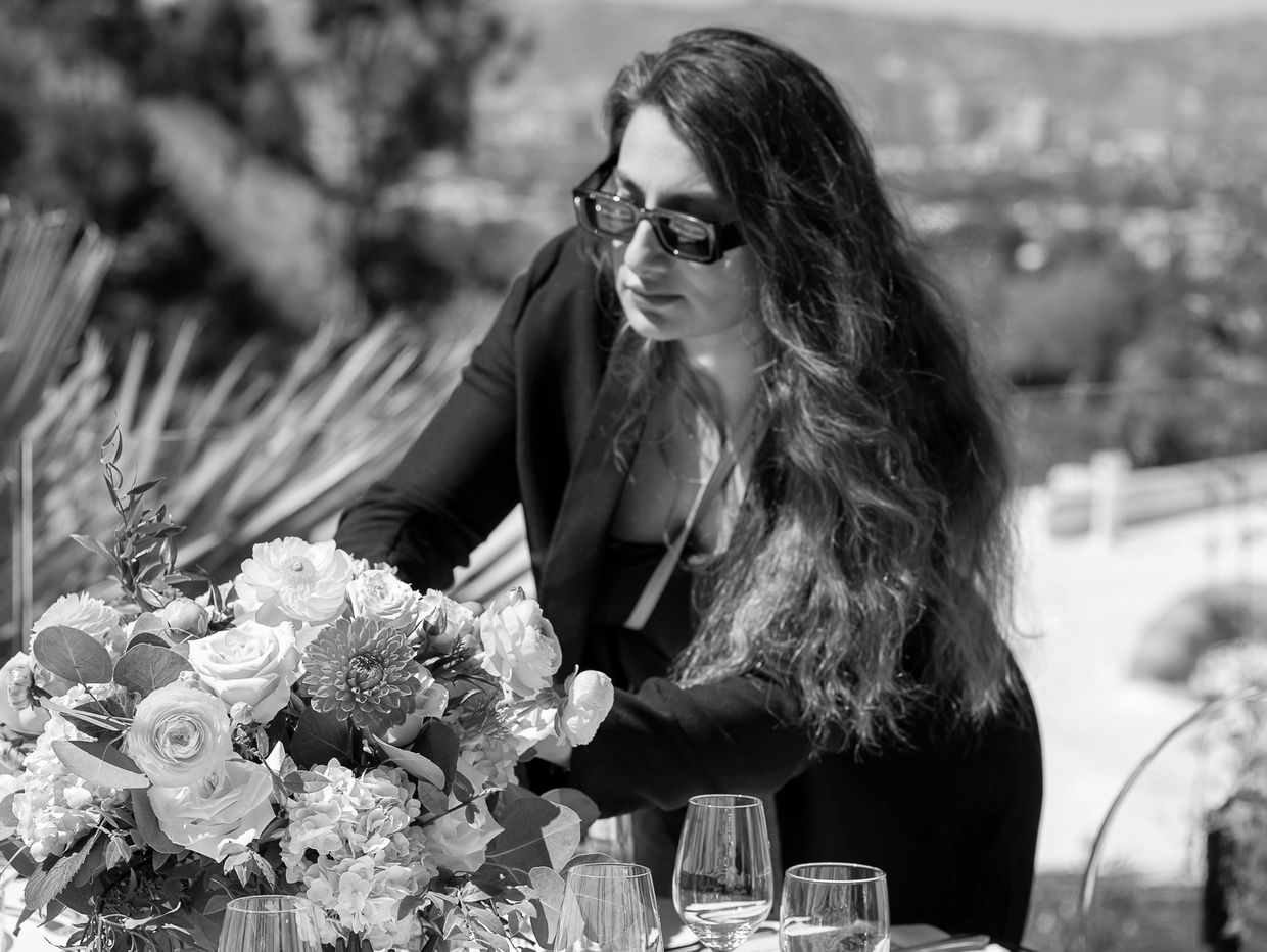 Woman arranging a colorful floral centerpiece outdoors. event planning, design, production