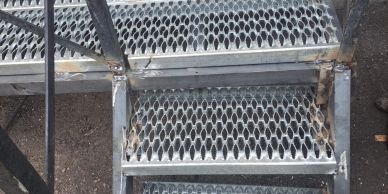 Metal grated stairs with a rusty frame on a concrete ground.