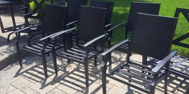 Black metal outdoor chairs lined on a tiled patio in sunlight.