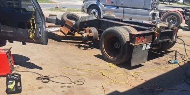 A truck chassis being repaired outdoors with tools and cables nearby.