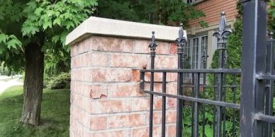 A brick pillar with a metal fence in a green outdoor setting.