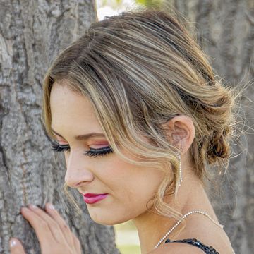 Woman with elegant makeup and hairstyle near tree.