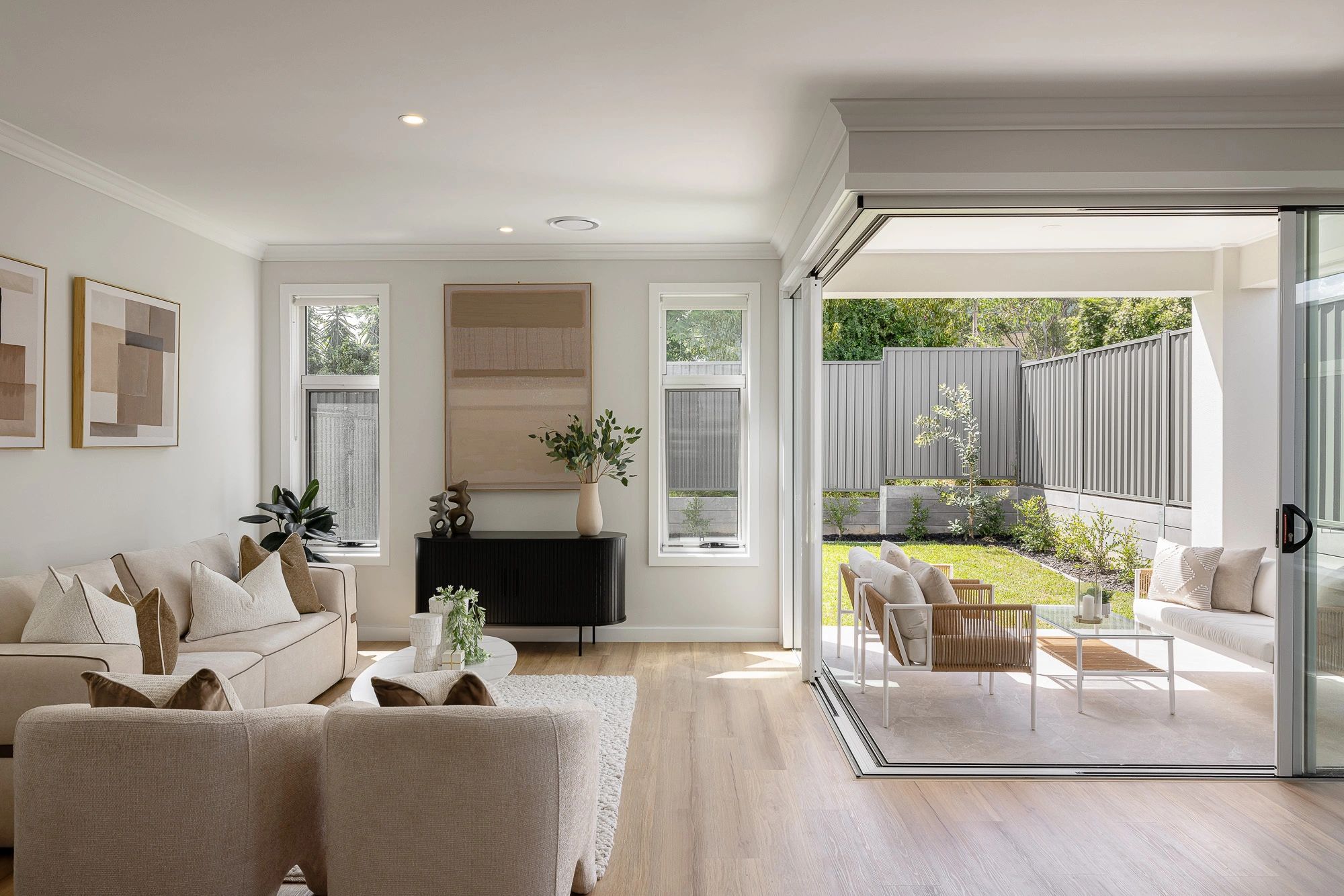 Bright, modern living room opens to a cozy outdoor patio with garden views.