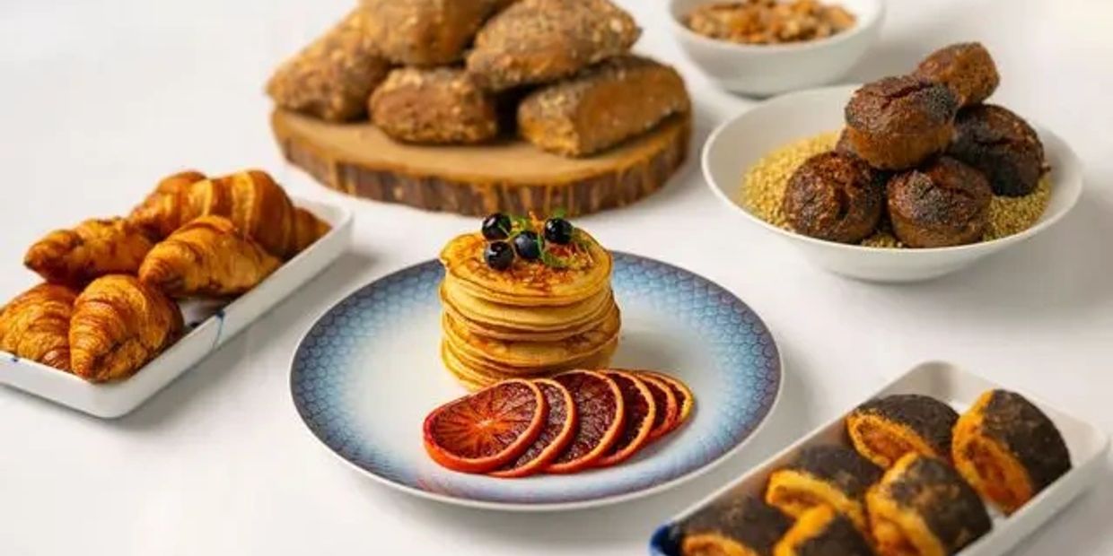 Variety of breakfast pastries and pancakes with fruit on a white table.