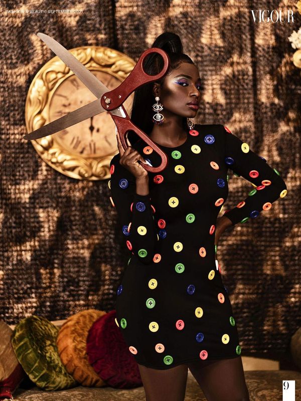 Woman in a black dress with colorful buttons holding giant scissors.