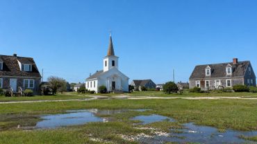 Small coastal village with a white church and traditional houses under a clear blue sky.