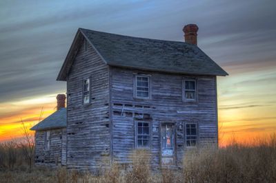 Abandoned weathered two-story house at sunset in a rural setting.