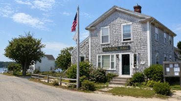 A quaint municipal hall building with an American flag in front on a sunny day.