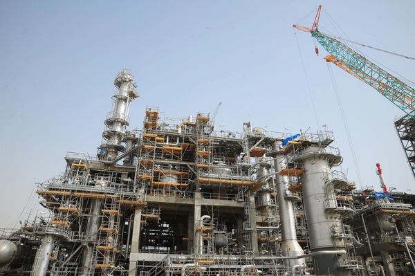 Industrial refinery under construction with scaffolding and cranes.