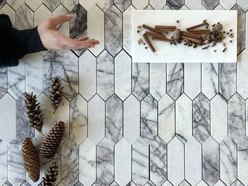 Hand gestures near pinecones and spices on a marble-patterned surface.