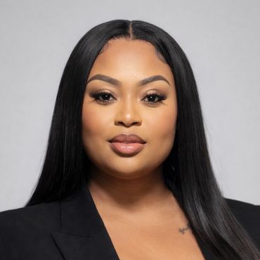 Professional headshot of a confident woman with long black hair and a black blazer.