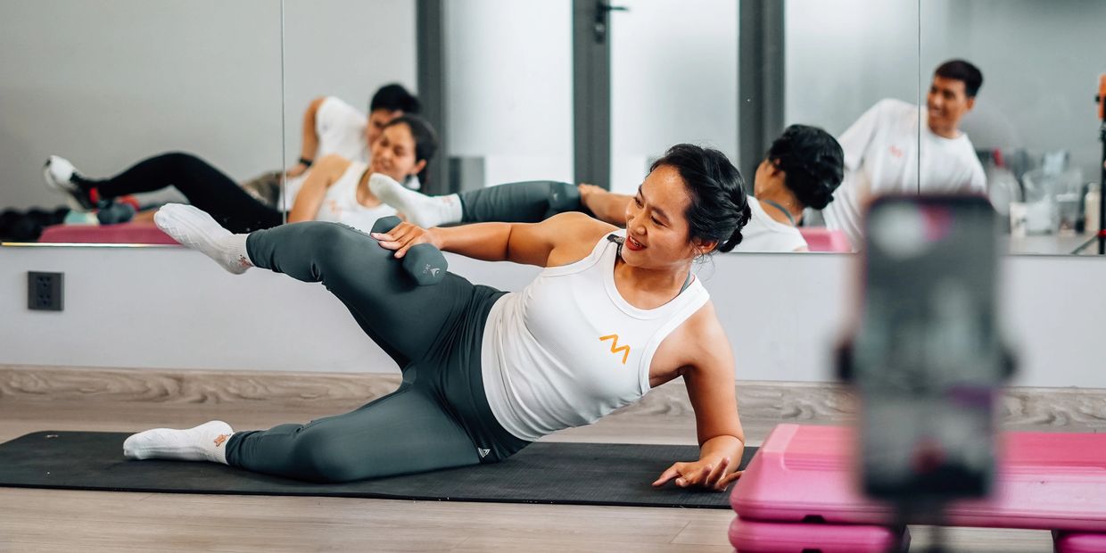 Woman exercising with leg raise and dumbbell on yoga mat in front of mirror.