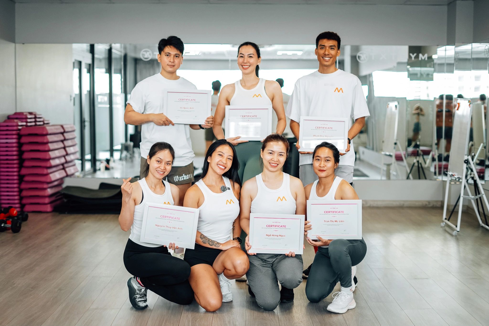 Group of six people holding certificates in a gym setting.