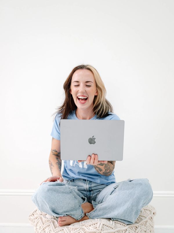 Young woman laughing while holding a laptop.
