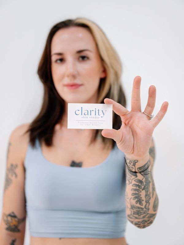 Woman holding a business card for Clarity Skin Studio.